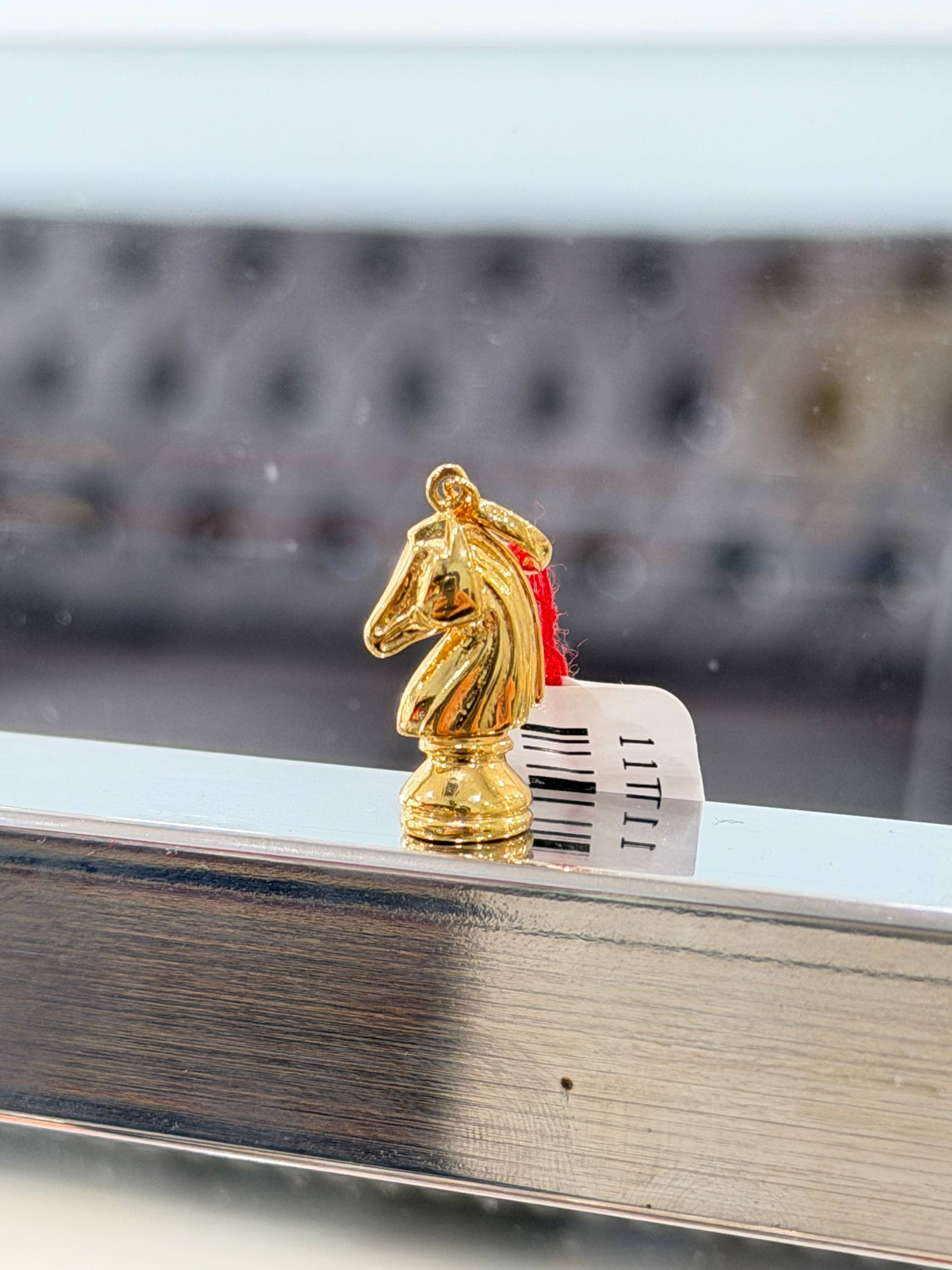Gold knight chess pendant piece on a reflective surface with a blurred background