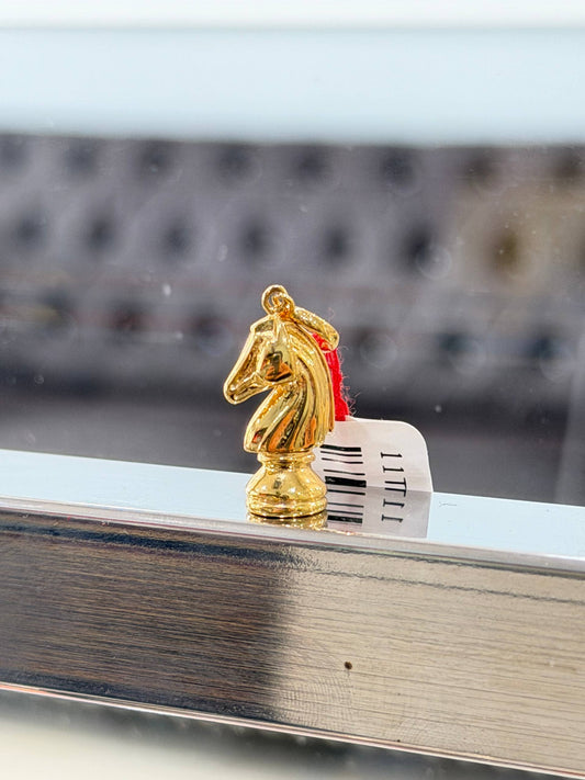 Gold knight chess pendant piece on a reflective surface with a blurred background
