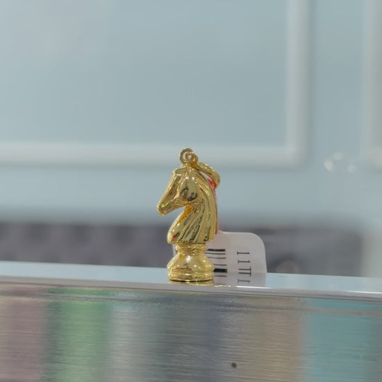 Gold knight chess piece pendant on a reflective surface with a blurred background