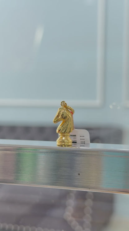 Gold knight chess piece pendant on a reflective surface with a blurred background